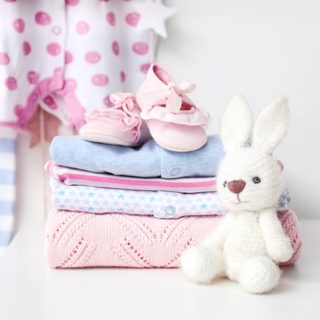 Baby,Clothes,With,Booties,And,Toy,On,Table,In,Room
